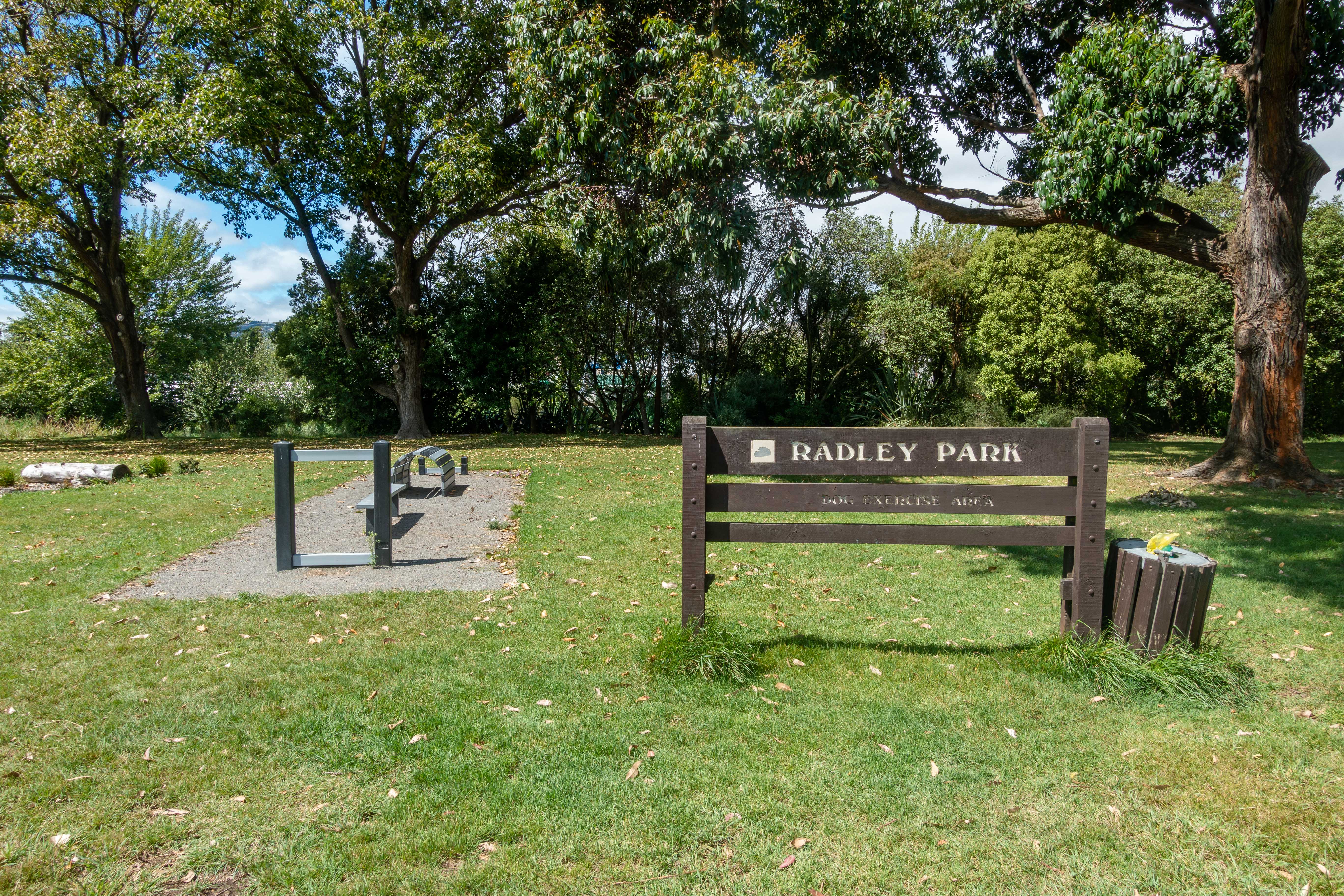A designated dog exercise area in a New Zealand park, with open grass, fencing, and a clear blue sky — Photo: Michal Klajban / CC BY-SA 4.0